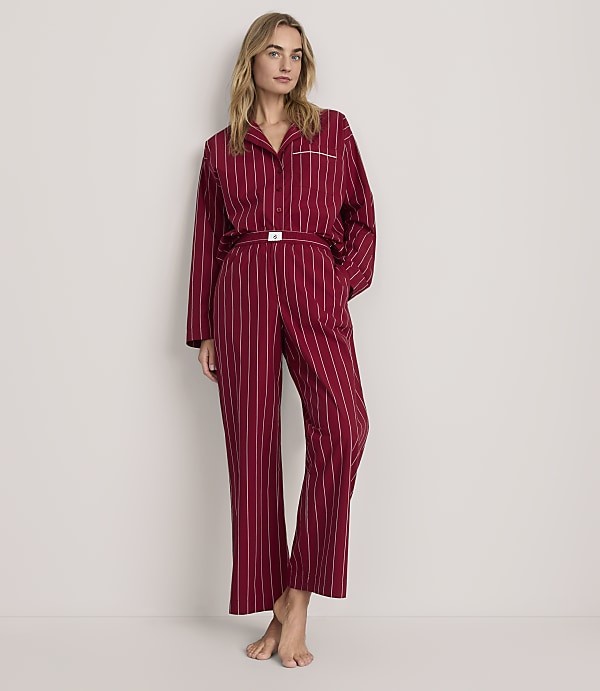 A woman wearing red striped pajamas stands against a plain, light-colored background.