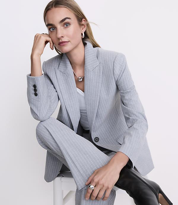 A woman wearing a light blue pinstripe suit and black boots sits against a plain white background.