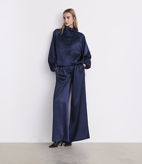 A woman wearing a navy blue satin two-piece outfit and black heels stands against a plain white wall.