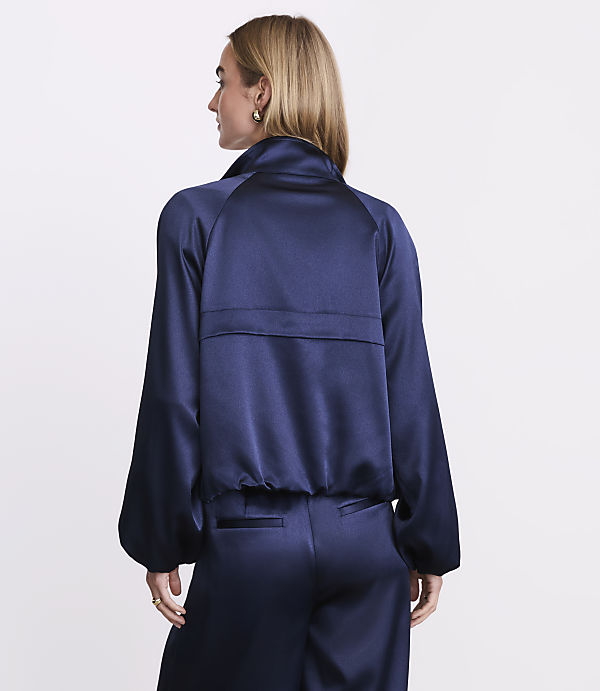 A woman with blonde hair wearing a navy blue satin outfit stands against a plain white background.