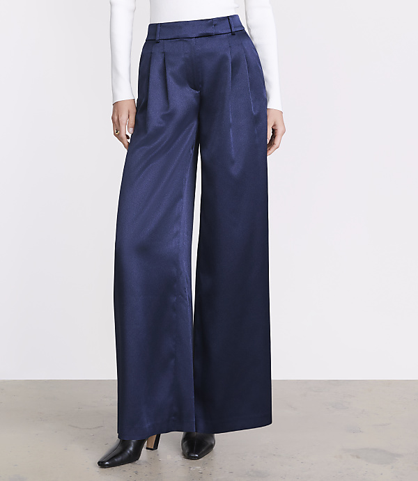 A person wears wide-leg navy blue trousers, a white long-sleeved top, and black pointed heels against a plain white background.
