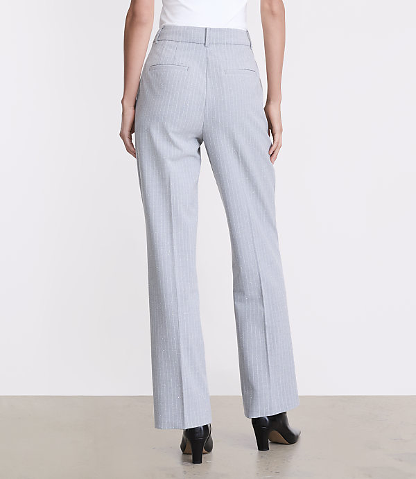 A person wearing light grey pinstriped trousers and black heels stands against a plain white background.
