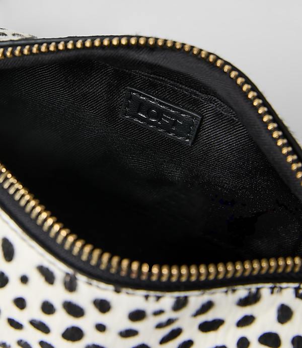 A white and black spotted pouch with a gold zipper and black interior is set against a plain light gray background.