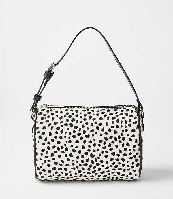 A white and black spotted handbag with a black strap sits against a plain, light gray background.