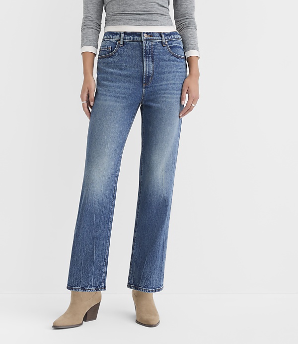 A person wearing high-waisted, straight-leg blue jeans and tan ankle boots stands against a plain white background.