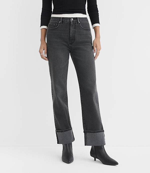 A person stands in the foreground wearing cuffed dark wash jeans and black boots against a plain white background.