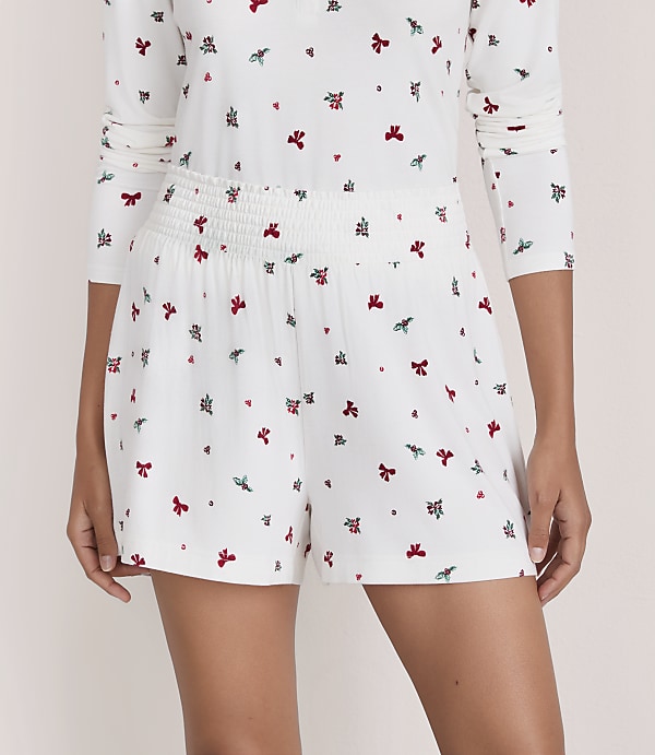 A person wears a white floral print pajama set against a plain, light-colored background.