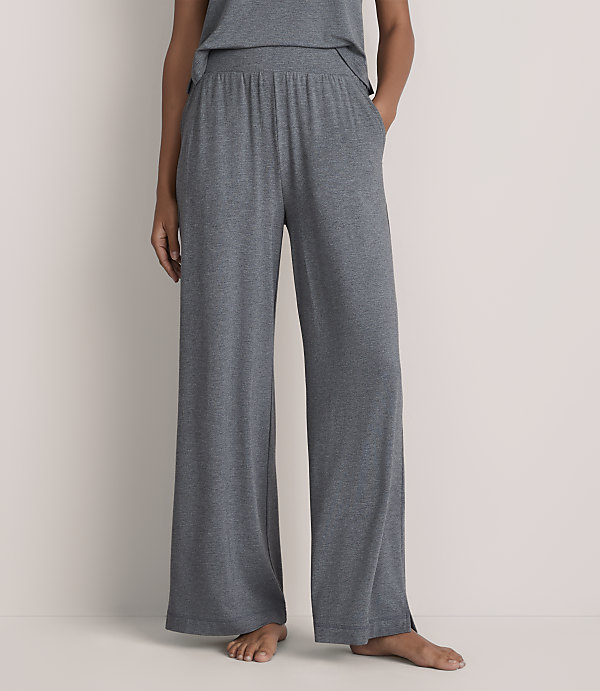 A person wearing wide-leg grey lounge pants stands against a plain, light-colored wall.