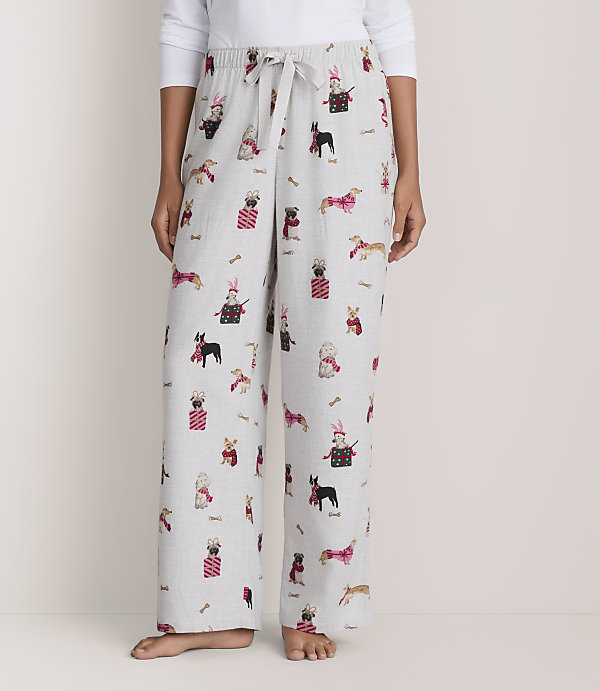 A person wears light gray pajama pants featuring a pattern of dogs against a plain white background.