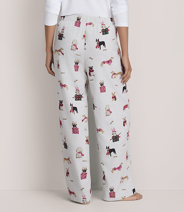 A person wears white pajama pants featuring a festive dog print against a plain, light-colored background.