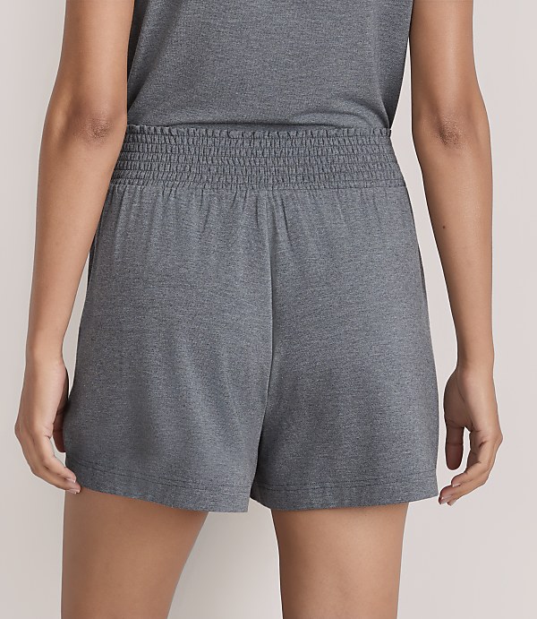 A person wears grey shorts and a matching top against a plain, light-colored background.
