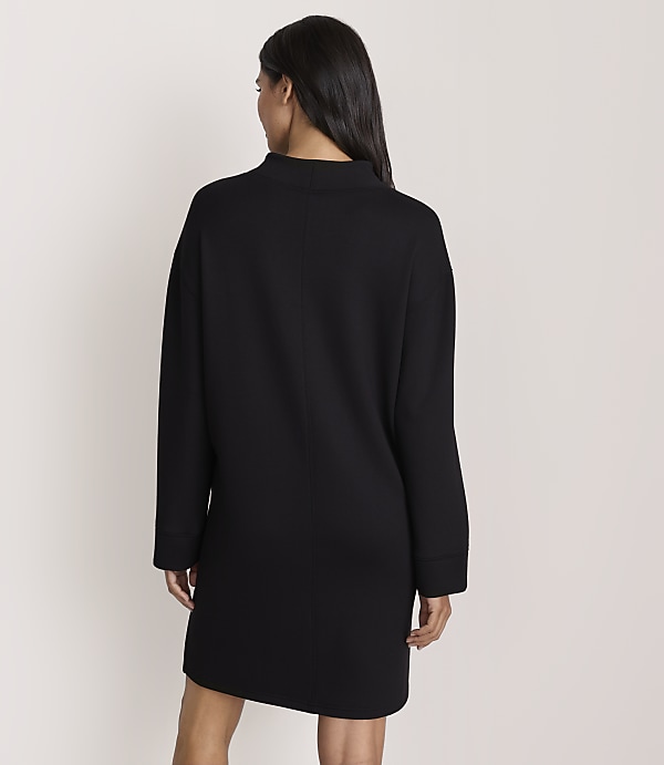 A woman wearing a long-sleeved black dress is seen from behind against a plain, light-colored background.