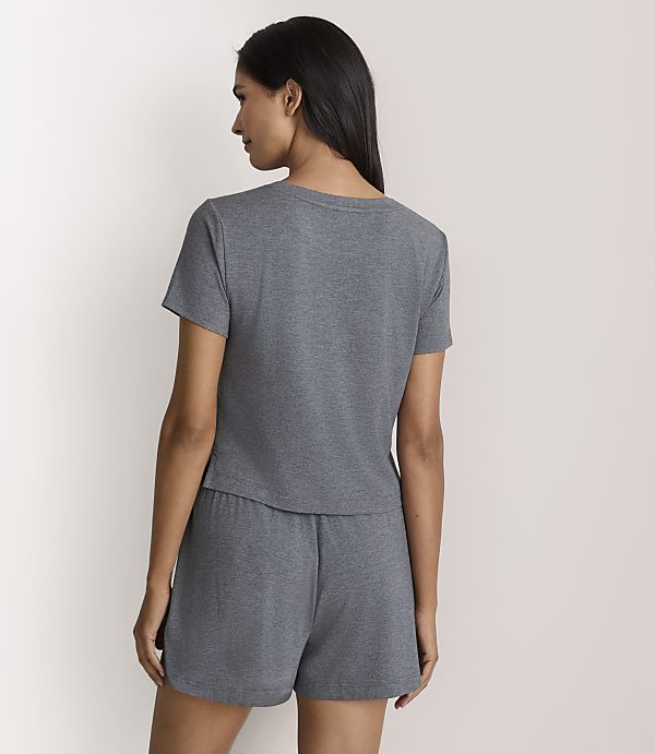 A woman wearing a grey short-sleeved t-shirt and matching shorts stands with her back to the camera against a plain white background.