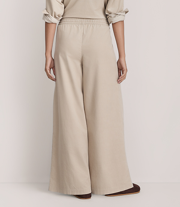 A person wearing wide-leg beige trousers and a matching top stands against a plain, light-colored background.