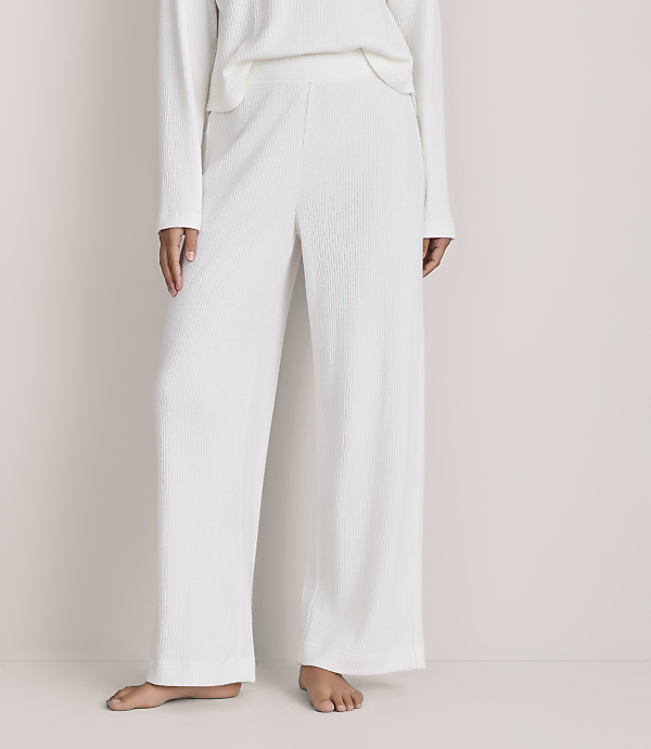 A person wearing a white ribbed knit matching set stands barefoot against a plain, light-colored background.