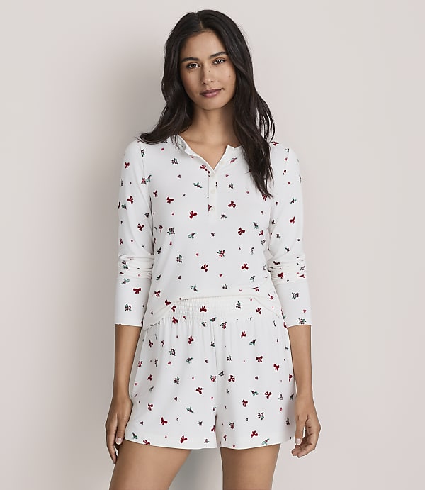 A woman wearing white floral print pajamas stands against a plain, light-colored wall.