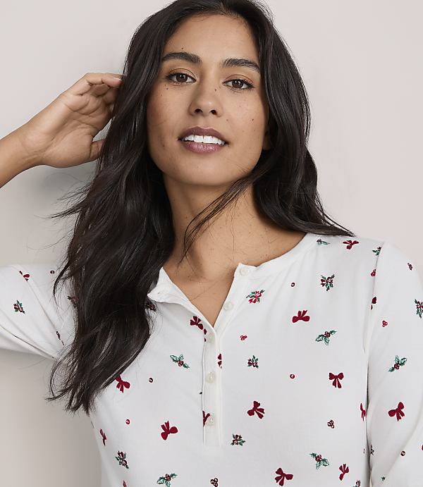 A woman with long dark hair wearing a white floral print shirt poses against a plain light-colored background.