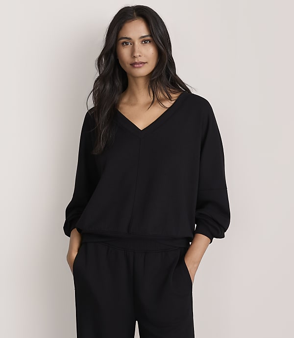 A woman wearing a black v-neck top and matching pants stands against a plain, light-colored background.