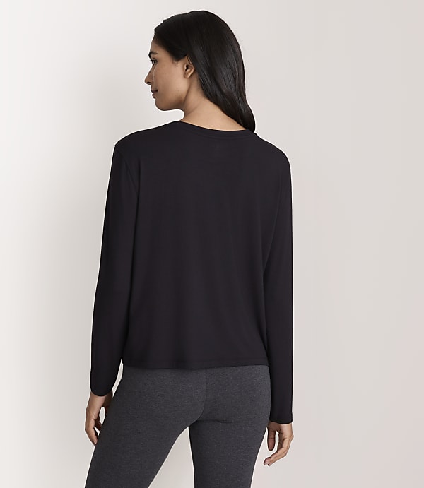 A woman wearing a black long-sleeved shirt and dark grey leggings stands against a plain white background.