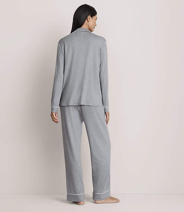 A woman stands with her back to the camera wearing grey pajamas against a plain, light-colored wall.