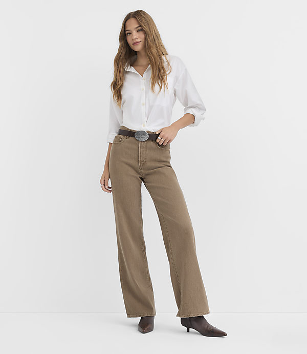 A woman in a white shirt and brown pants stands against a plain white background.