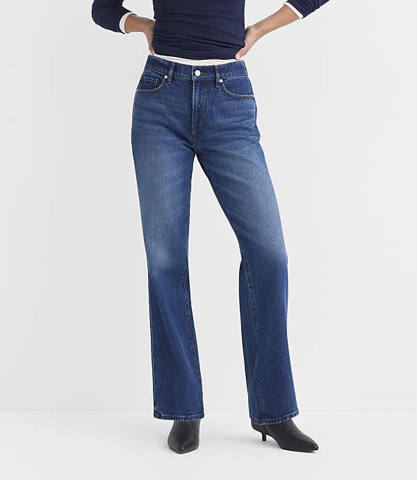 A person wearing blue flared jeans and black heeled boots stands against a plain white background.