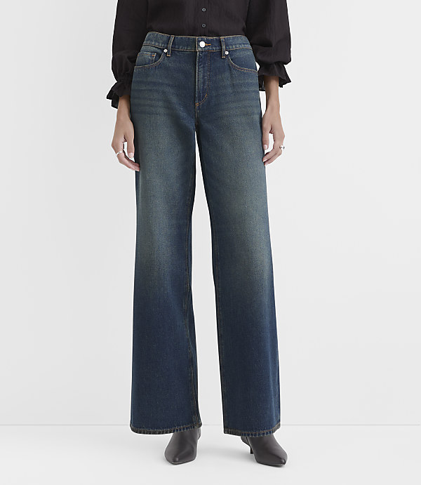 A person wearing a black blouse and wide-leg blue jeans stands against a plain white background.