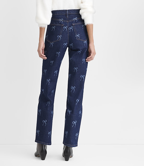 A person wearing a white fuzzy sweater and dark blue jeans with light blue bow patterns stands against a plain white background.