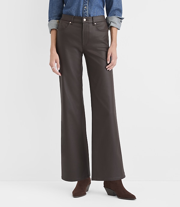 A person wearing a blue denim shirt, dark brown wide-leg trousers, and brown suede boots stands against a plain white background.
