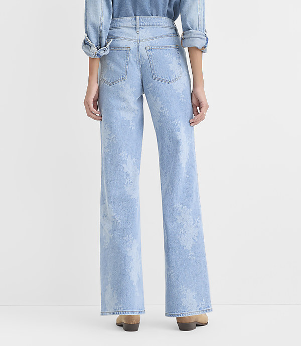 A person wearing a denim shirt and light-wash floral print wide-leg jeans stands against a plain white background.