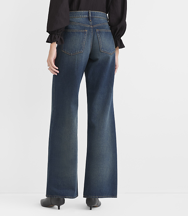 A person wearing a black top and wide-leg blue jeans stands against a plain white background.