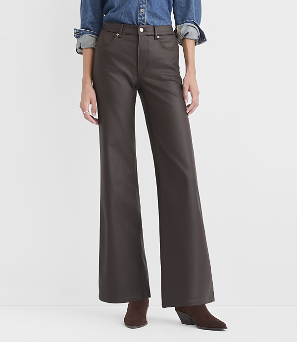 A person wearing a blue denim shirt and wide-leg brown faux-leather trousers stands against a plain white background.