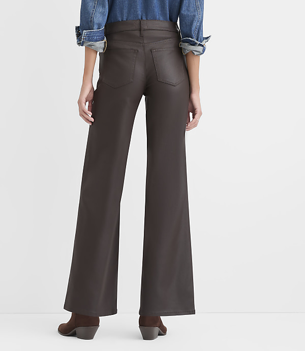 A person wearing a blue denim shirt and brown wide-leg faux leather pants stands against a plain white background.