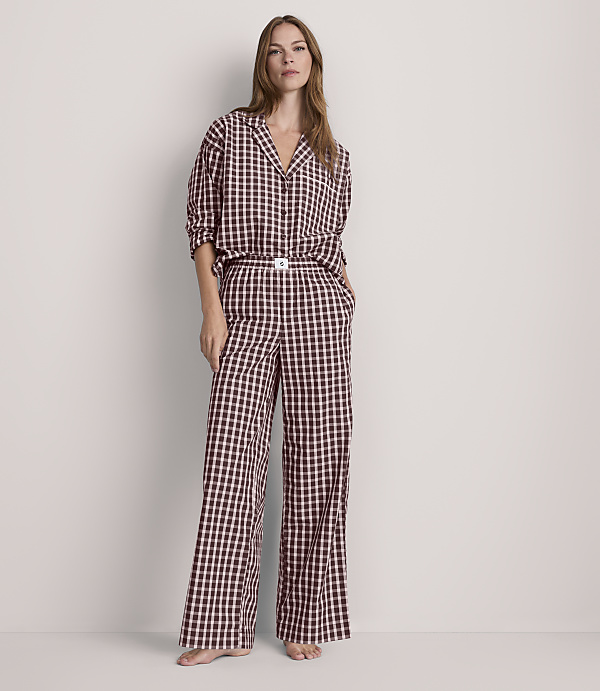 A woman stands in a light-colored room wearing a black and white checkered pajama set, with her hands in her pockets.