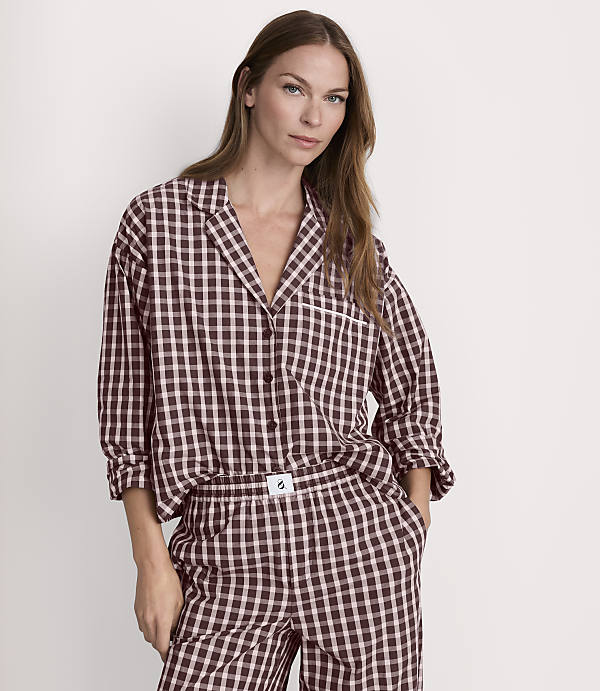 A woman in brown and white checkered pajamas stands against a plain white background.