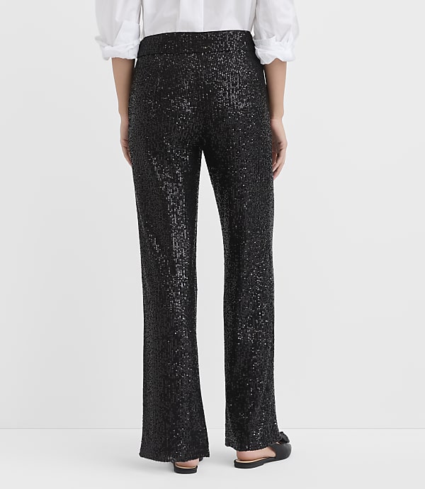 A person stands with their back to the camera wearing a white blouse and black sequined trousers against a plain white background.