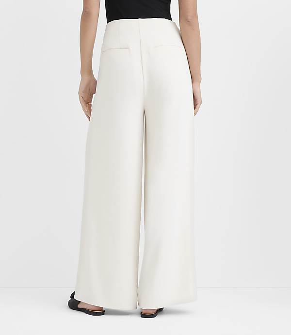 A person wearing a black top and wide-leg white trousers stands against a plain white background.