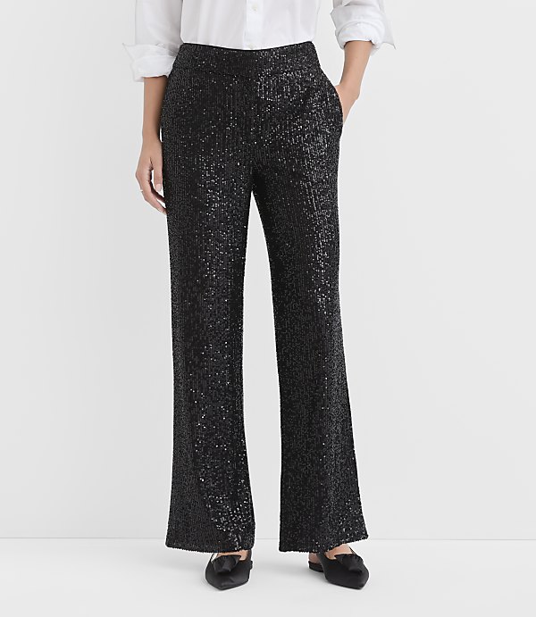 A person wears a white button-down shirt and shimmering black sequined trousers against a plain white background.