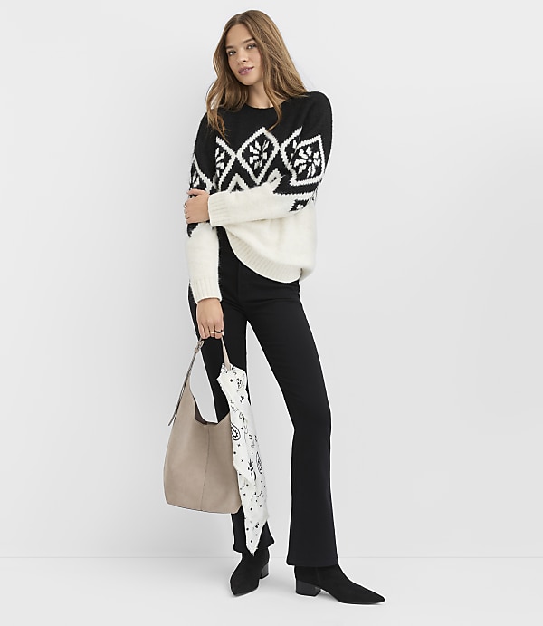 A woman wearing a black and white patterned sweater and black pants stands against a plain white background.