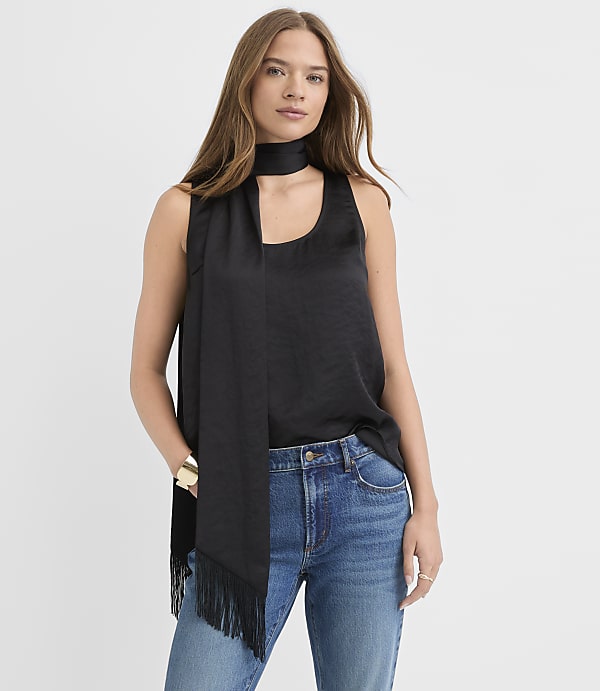 A woman wearing a black sleeveless top, a black scarf, and blue jeans stands against a plain white background.