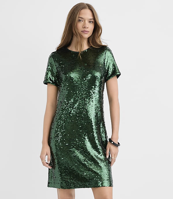 A woman wearing a short-sleeved green sequin dress stands against a plain white background.