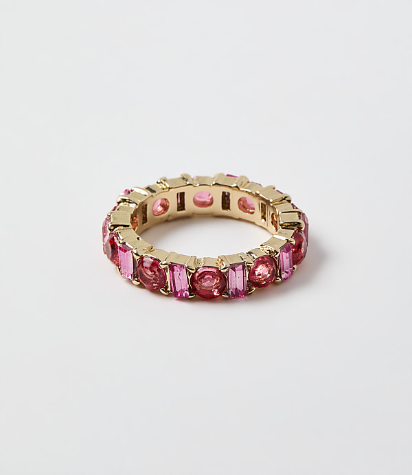 A gold ring set with pink gemstones rests on a plain white background.