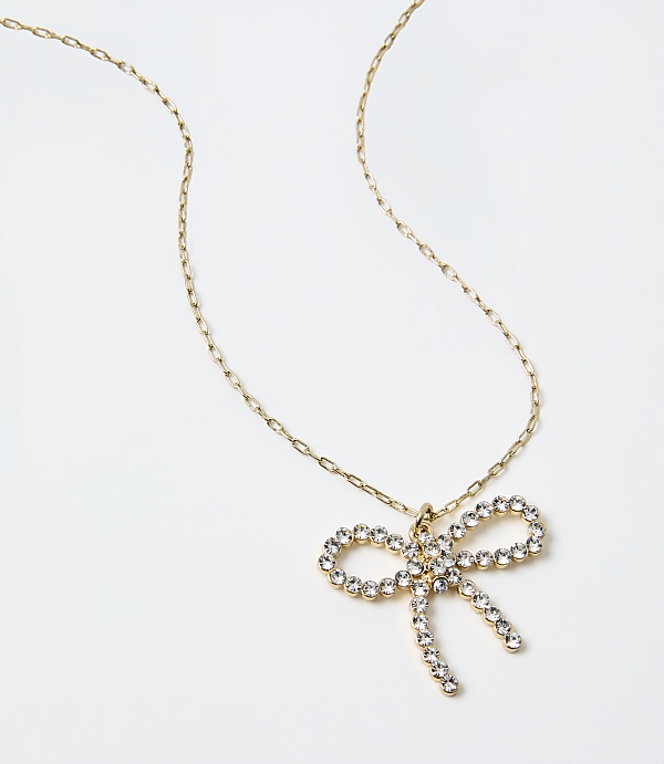 A gold chain necklace with a sparkling bow-shaped crystal pendant rests on a plain white background.