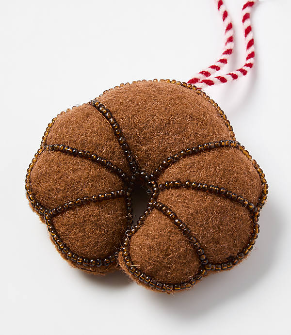 A brown felt pastry ornament with bead detailing and a red-and-white string sits against a plain white background.