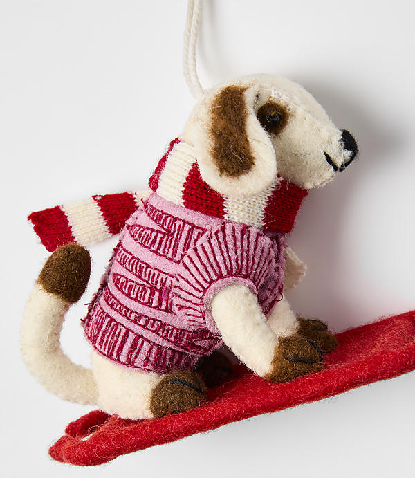 A small felt dog wearing a pink and red striped sweater stands on a red sled against a plain white background.