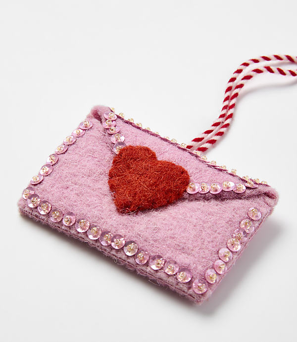 A pink felt envelope with a red heart and sequins sits on a plain white background.