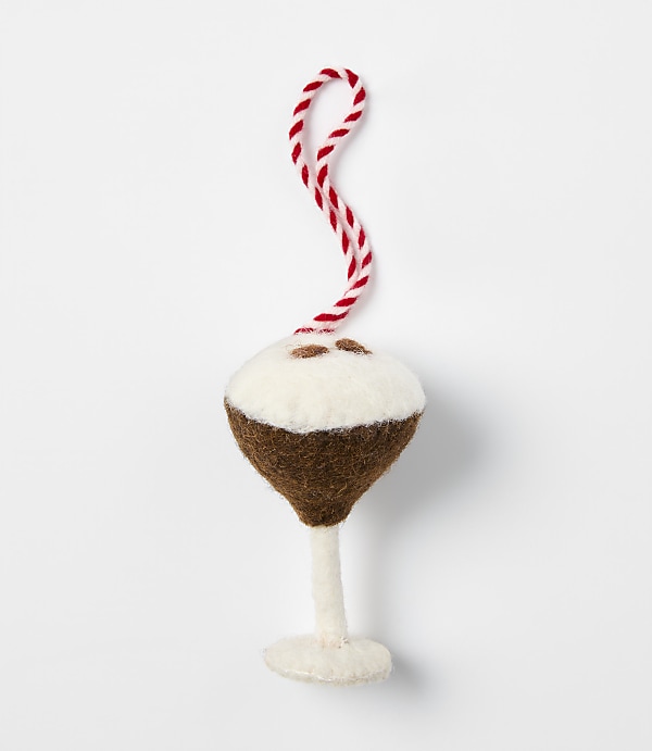 A felt ornament shaped like a cocktail glass with a brown drink and white foam sits against a plain white background.