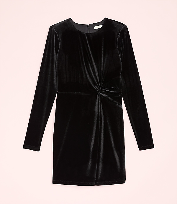 A long-sleeved black velvet dress with a twisted waist detail is centered against a pale pink background.