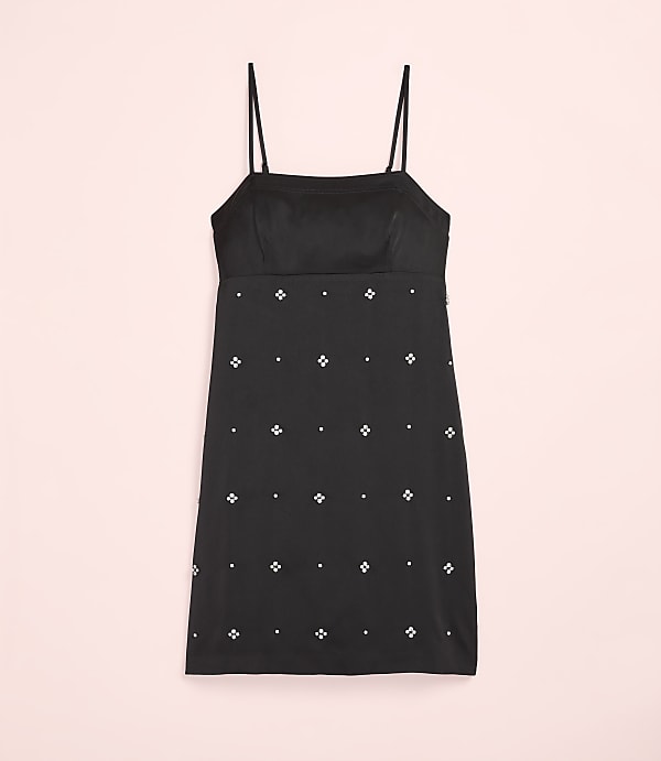 A black mini dress with small white floral embellishments is centered against a plain light pink background.