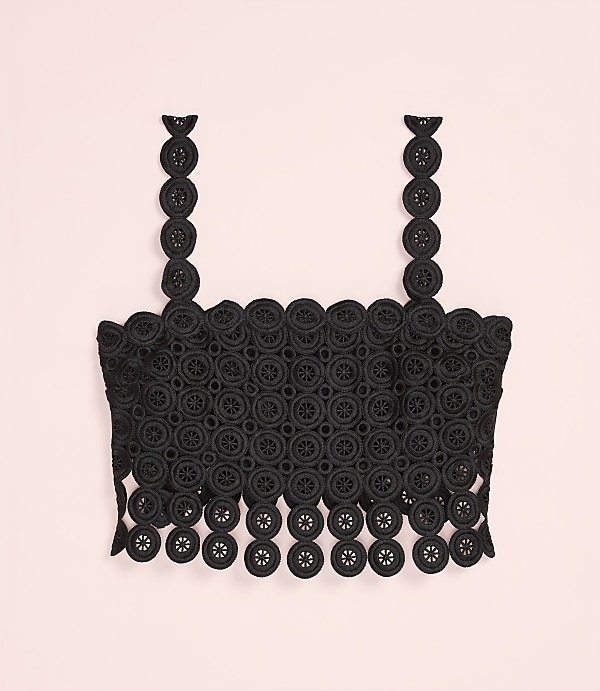 A black lace crop top with circular patterns is centered against a plain light pink background.